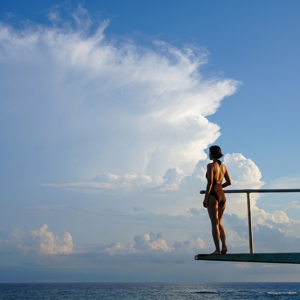 Diving board over open water, pure white sky, minimal figure