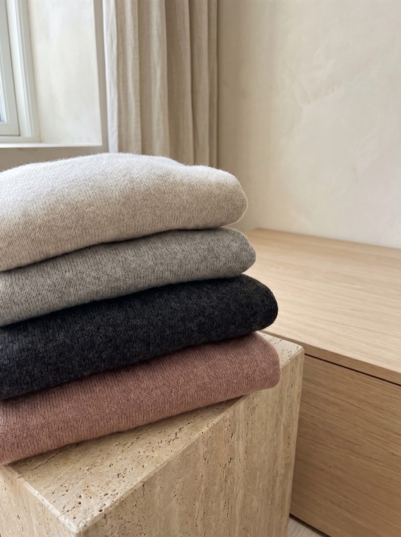 A folded stack of premium knitwear on warm stone in soft editorial daylight