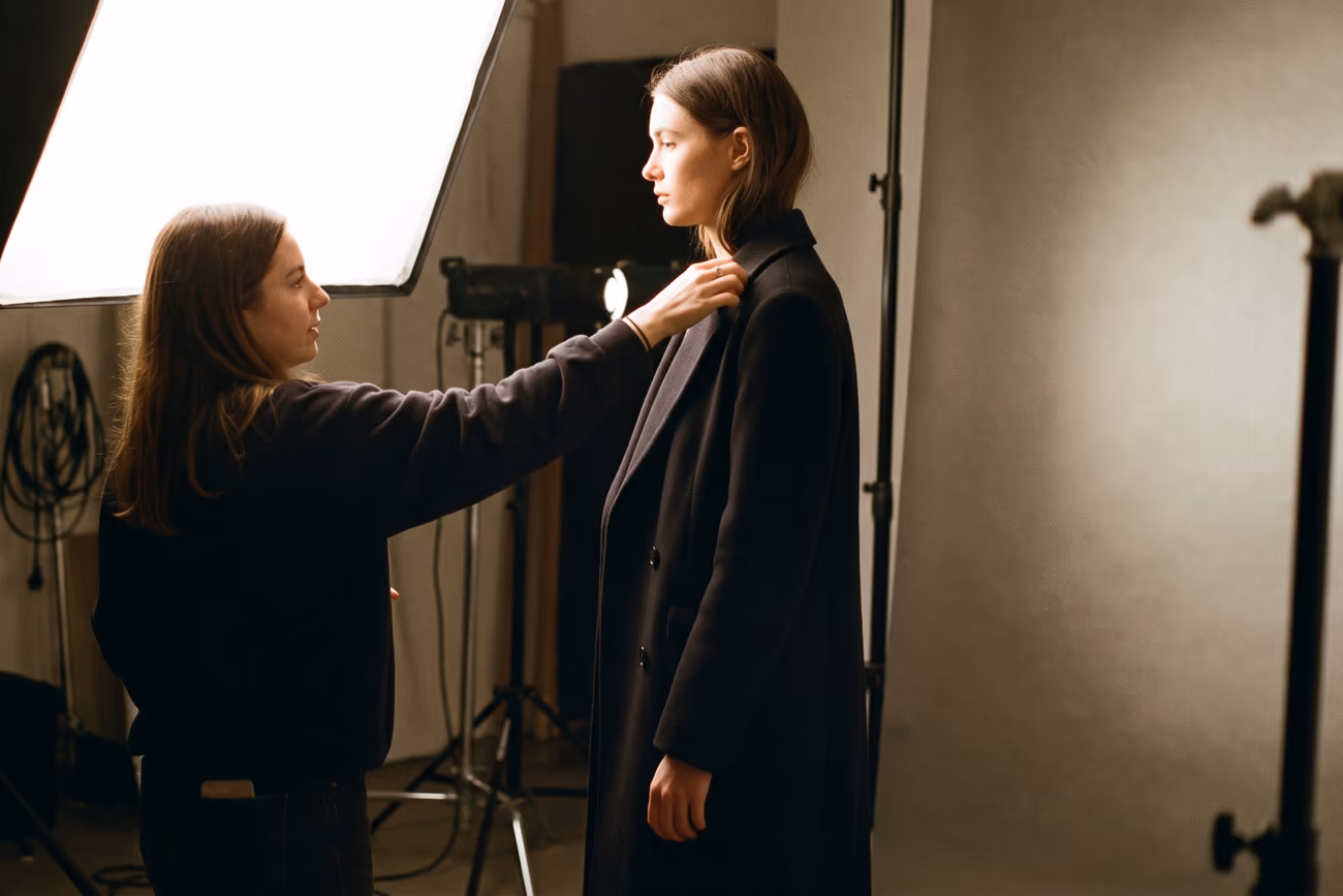 A stylist adjusting a model's collar under studio strobes
